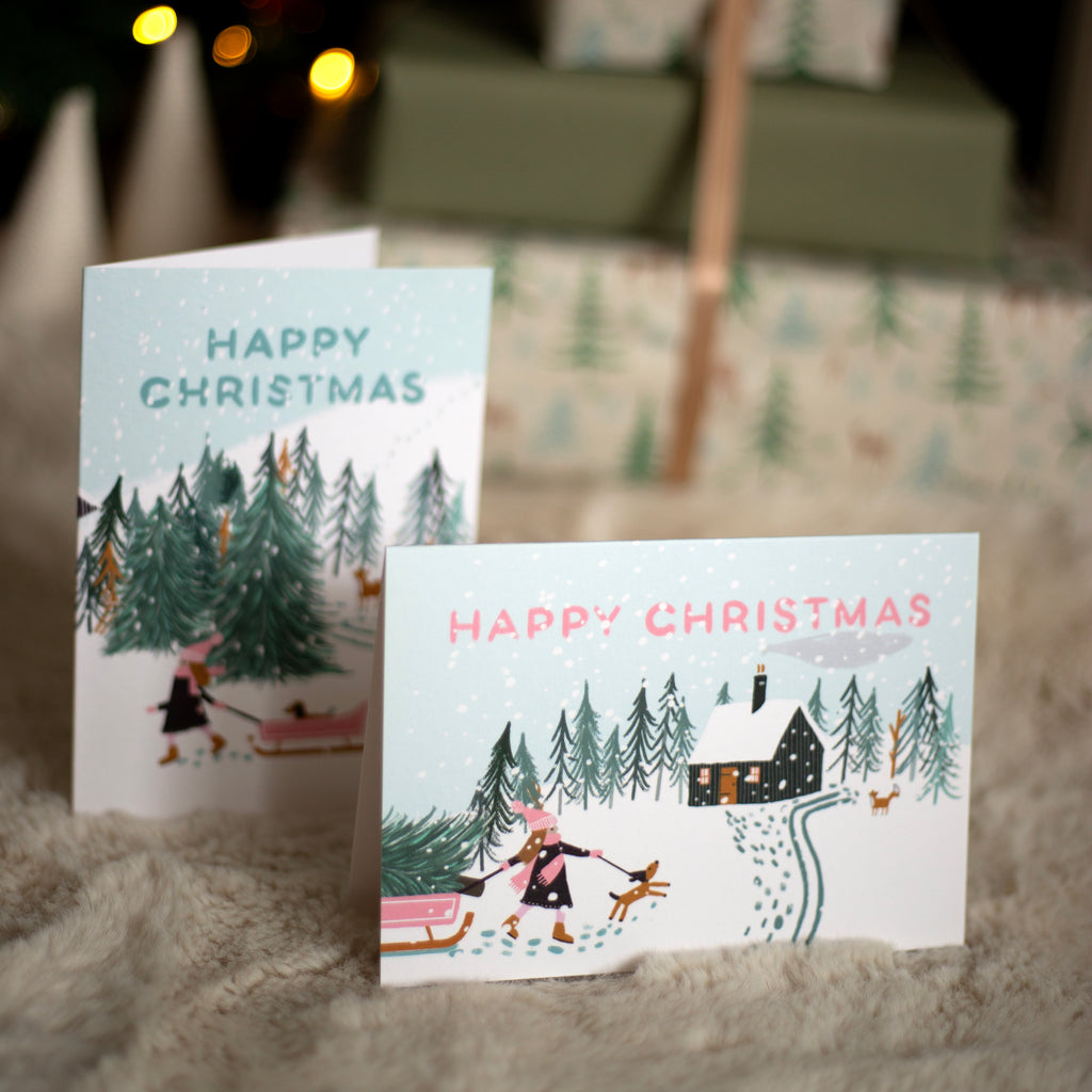 Two Christmas cards with winter scenes and 'Happy Christmas' text on a textured surface.