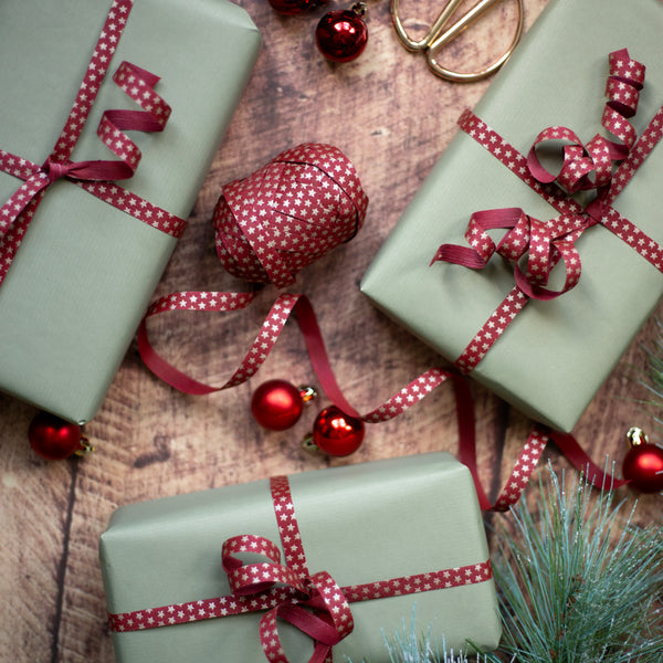 Three wrapped gifts with red curling ribbons on a wooden surface with Christmas decorations.
