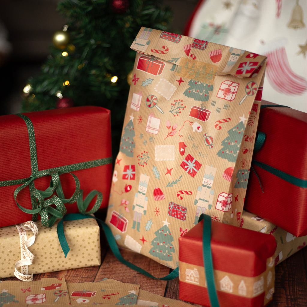 Stack of Christmas presents with patterned gift bag and ribbons in front of a decorated tree.