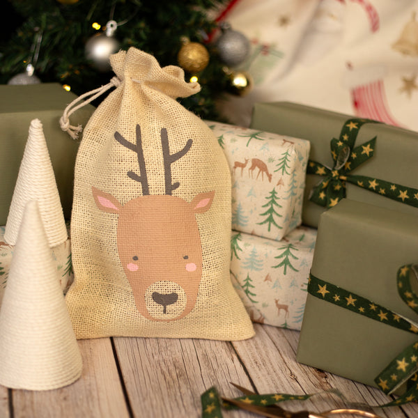 Burlap sack with reindeer design on a wooden surface with Christmas decorations.
