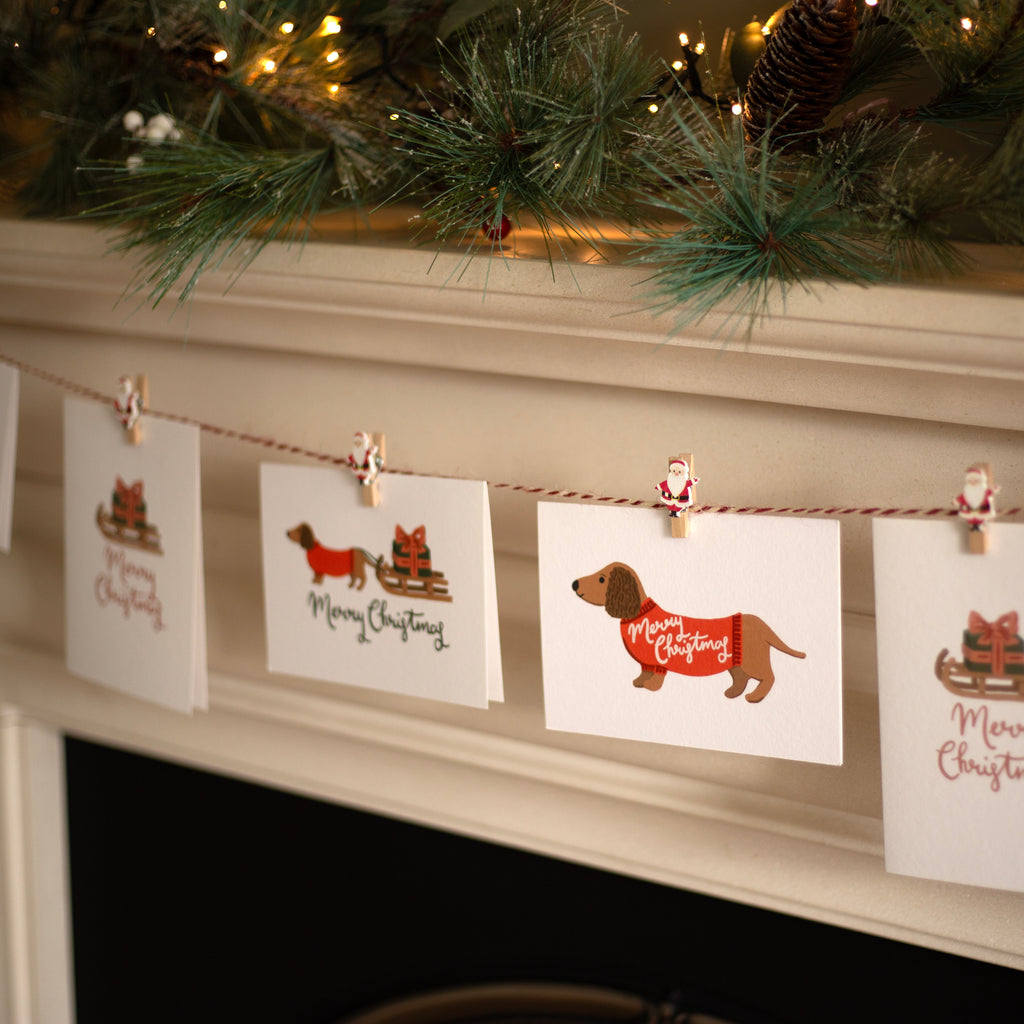 Christmas-themed cards with dogs and 'Merry Christmas' text on a string with clips, against a festive background.