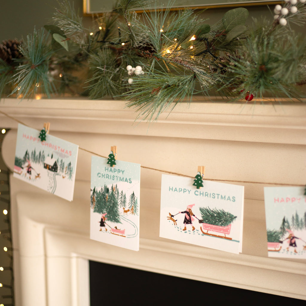 Christmas cards hanging on a string with clips against a decorated fireplace.