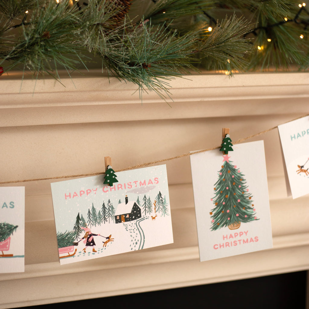 Christmas cards with festive designs hanging on a string against a fireplace.