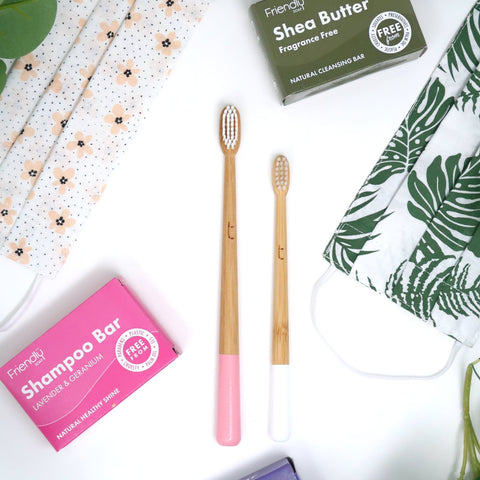 colourful bamaboo toothbrushes and shampoo bars laid out on a white surface surrounded by flowers