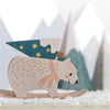 Wooden polar bear figurine with a hat and scarf on a snowy surface with blurred trees in the background
