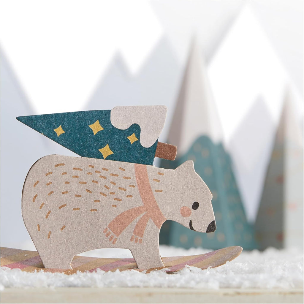 Wooden polar bear figurine with a hat and scarf on a snowy surface with blurred trees in the background