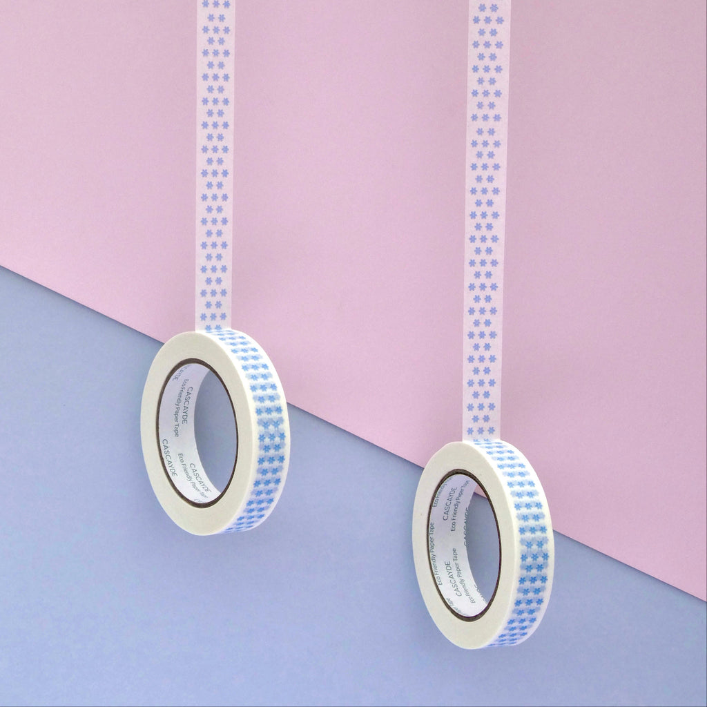 Two rolls of washi tape with a blue and white floral pattern, hanging vertically against a split pastel pink and lavender background.