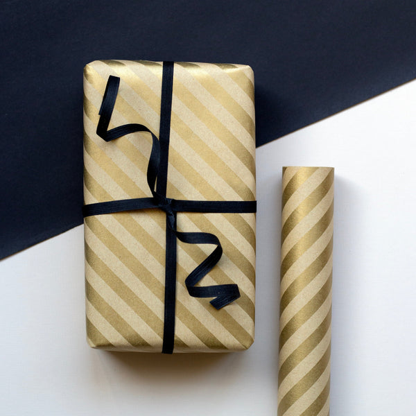 Gift box wrapped in gold striped paper with black ribbon on a white surface