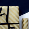 Gift wrapped in gold and white striped paper with a black ribbon on a dark background