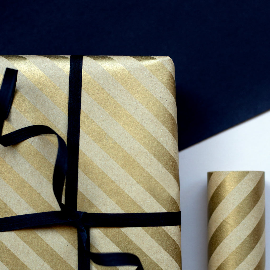 Gift wrapped in gold and white striped paper with a black ribbon on a dark background