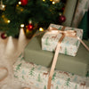 Wrapped Christmas presents with festive paper and ribbons in front of a decorated tree.