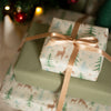 Gift box with deer and tree pattern wrapped in festive paper with a gold ribbon.