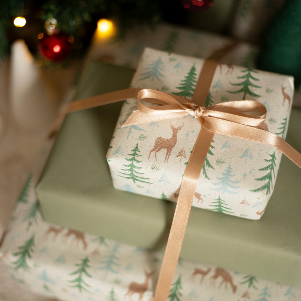 Gift box with deer and tree pattern wrapped in festive paper with a gold ribbon.