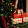 Stack of Christmas presents with red ribbons near a decorated tree.