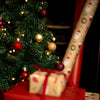 Christmas tree with decorated ornaments and wrapped presents next to a roll of Santa Claus-themed wrapping paper.