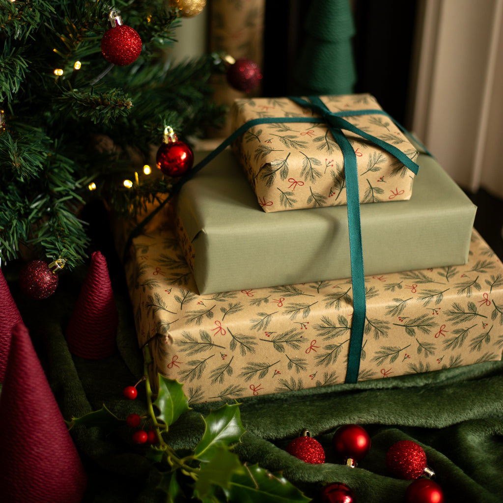 Stack of Christmas presents wrapped in patterned paper with ribbons near a decorated tree.