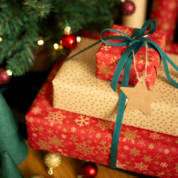 Stack of Christmas presents under a decorated tree with red and gold snowflake wrapping.