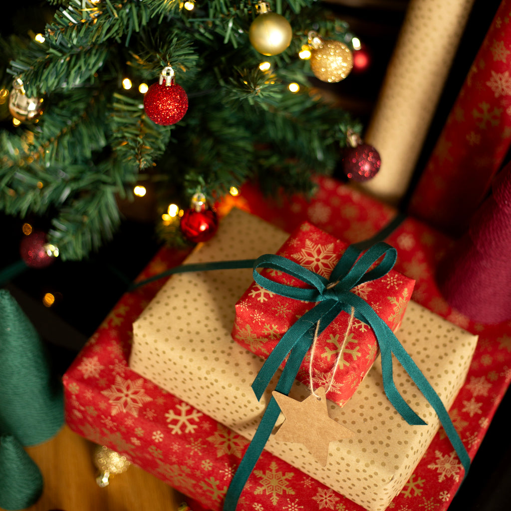 Gifts under a decorated Christmas tree with red and gold snowflake paper and green ribbon.