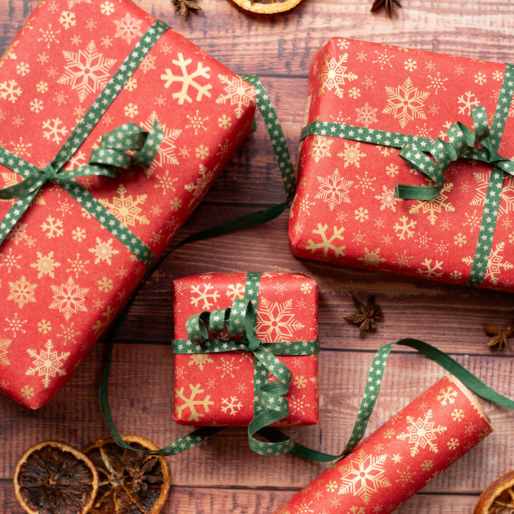 Red gift boxes with gold snowflake patterns and green ribbons on a wooden surface.