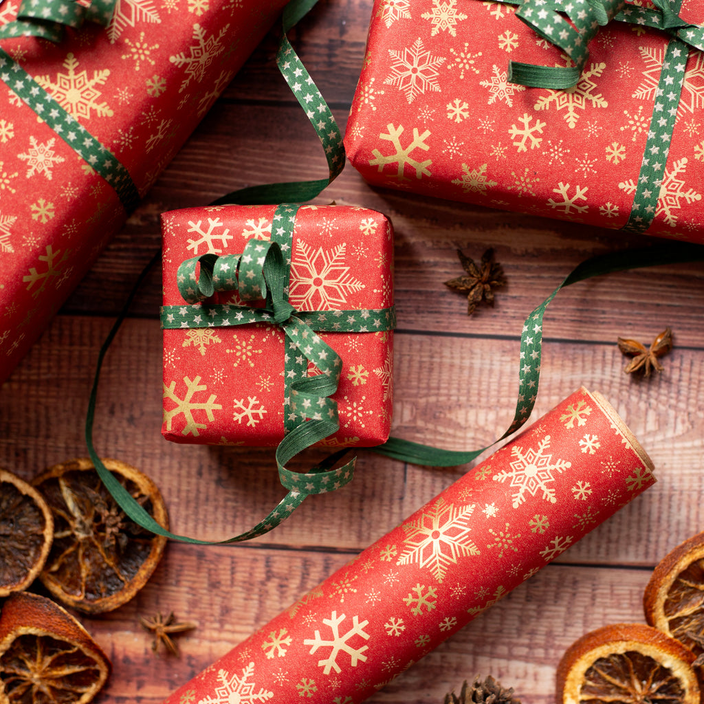 Red gift boxes with gold snowflake patterns and green ribbons on a wooden surface with dried oranges and star anise.