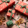 Red gift boxes with green ribbons on a wooden surface with dried oranges and star anise.