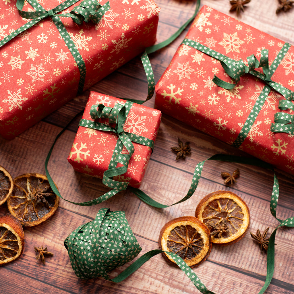 Red gift boxes with green ribbons on a wooden surface with dried oranges and star anise.