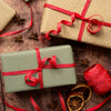 Two gift boxes tied with red ribbons on a rustic wooden surface with star anise and dried oranges.