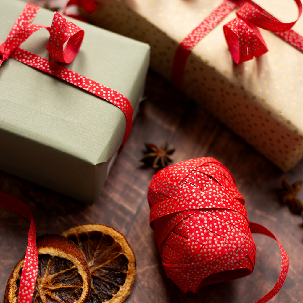 Gift boxes with red ribbons and a spool of red curling ribbon on a wooden surface.