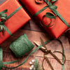 Two red gift boxes with green ribbons on a wooden surface, accompanied by scissors and additional green ribbon.