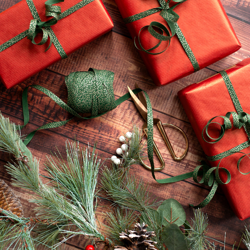 Red gift boxes with green curling ribbons on a wooden surface with Christmas decorations.