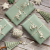 Three green gift boxes with ribbons on a wooden surface, surrounded by festive decorations.