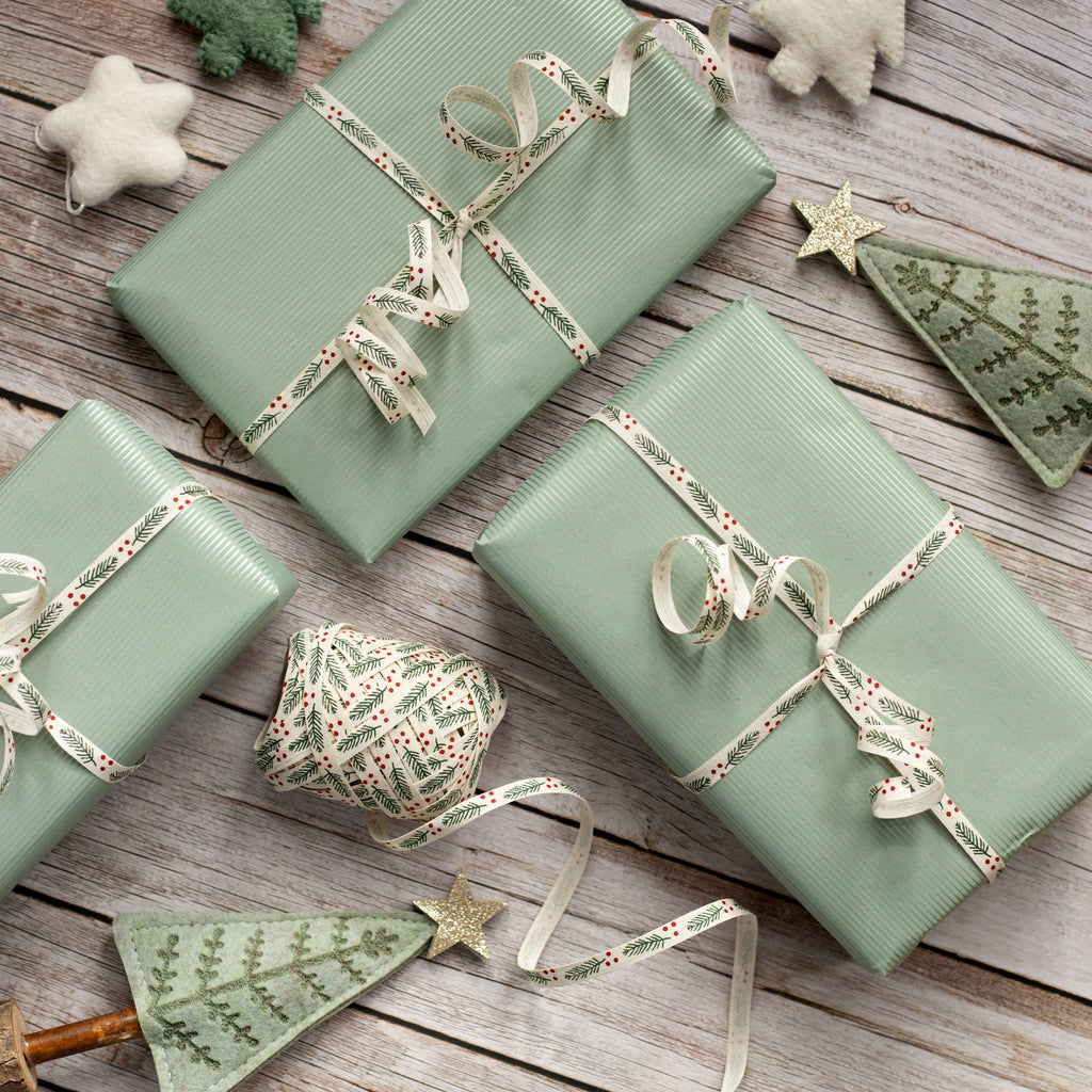 Three green gift boxes with ribbons on a wooden surface, surrounded by festive decorations.