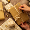 Person curling a ribbon on a wrapped gift with other gifts and decorative items in the background.