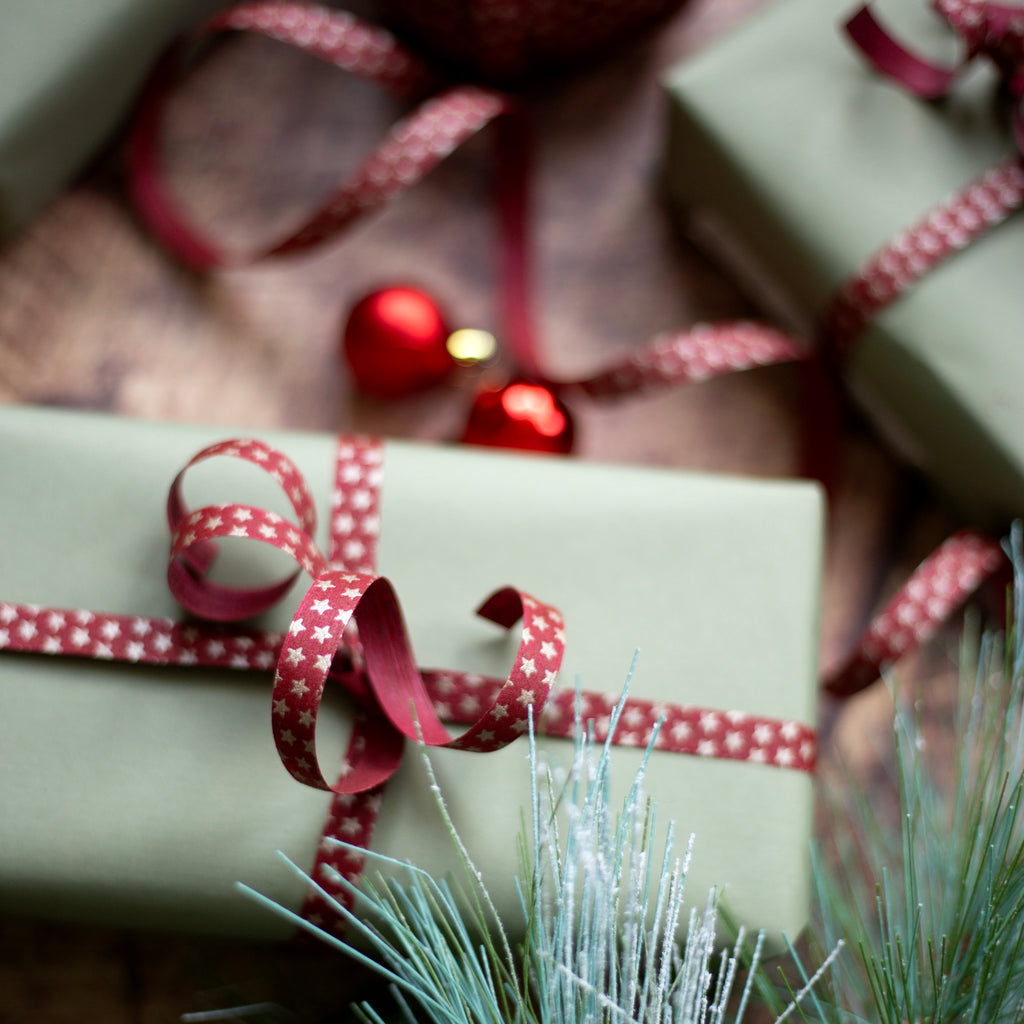 Close-up of wrapped Christmas presents with red star ribbons and pine branches.