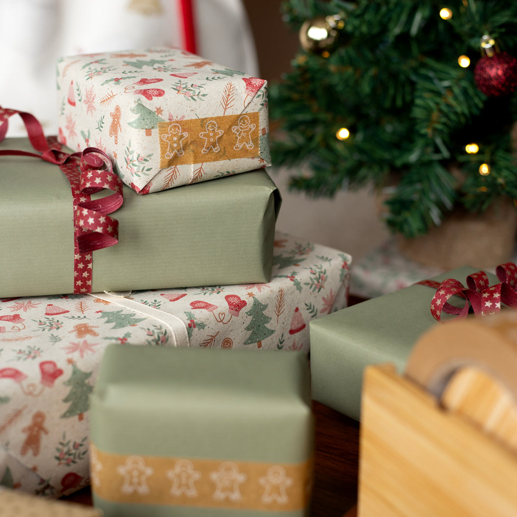 Stack of Christmas presents with festive wrapping paper in front of a decorated tree.