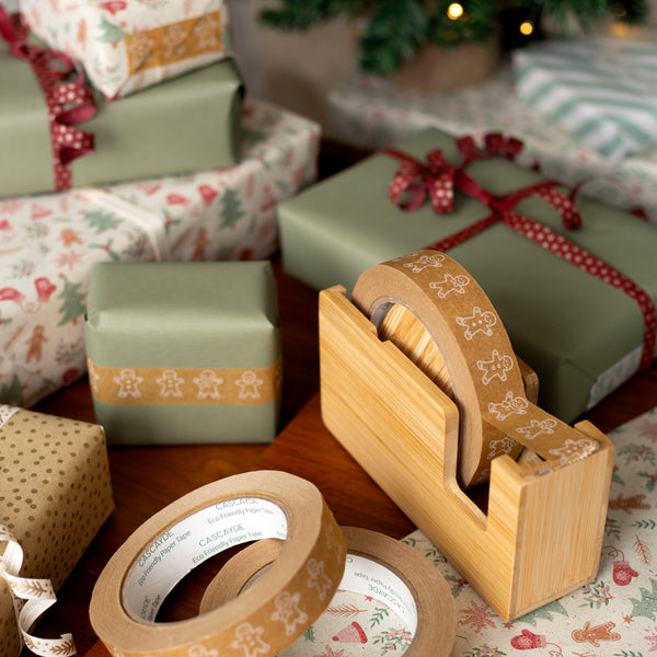 Wooden tape dispenser with gingerbread men tape on a table with wrapped Christmas gifts in the background
