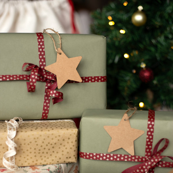 Christmas presents wrapped in green paper with red ribbons and star-shaped tags, against a blurred Christmas tree background.