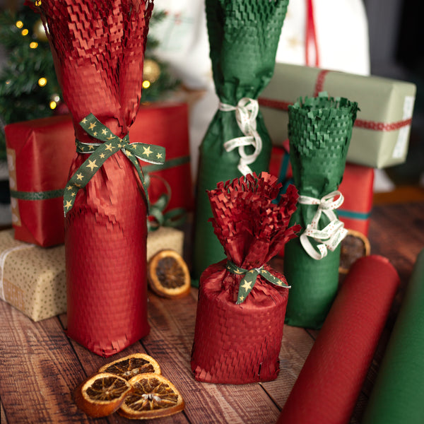Decorative bottles wrapped in red and green honeycomb paper with ribbons on a wooden surface.