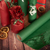Green honeycomb paper roll on a wooden surface with red gift bags and decorative elements.