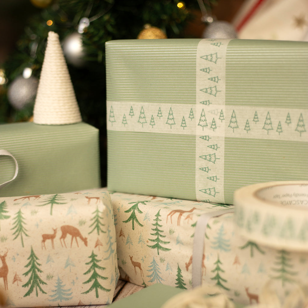 Gift boxes with Christmas Tree & Reindeer designs in front of a Christmas tree.