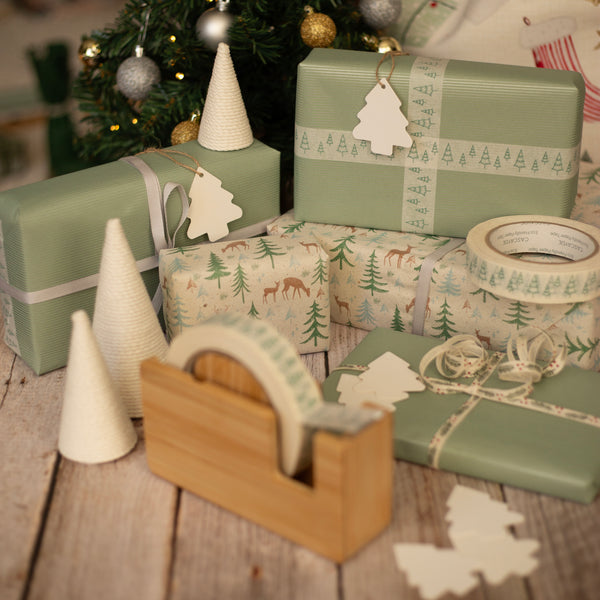 Christmas gift wrapping with green boxes, decorative tape, and tree-shaped cones on a wooden surface.
