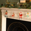 Decorative Christmas garland with Santa, reindeer, Nutcracker and fairy puppets on a fireplace mantel.