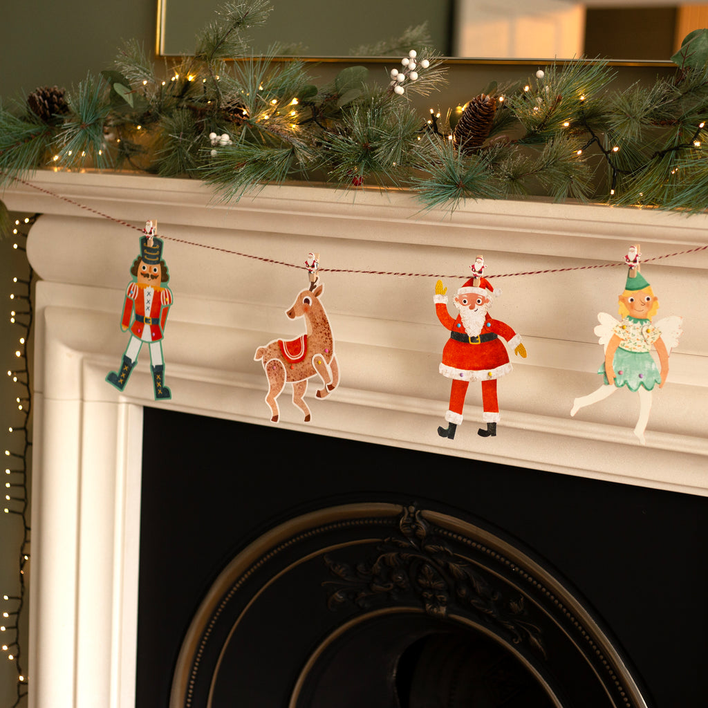 Decorative Christmas garland with Santa, reindeer, Nutcracker and fairy puppets on a fireplace mantel.