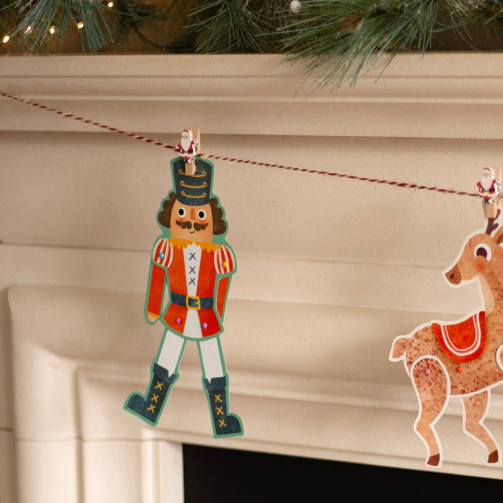 Decorative Christmas ornaments of a nutcracker and a reindeer hanging on a string against a neutral background.