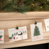 Christmas cards with festive designs hanging on a string against a fireplace.