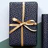 Navy blue gift box with gold polka dots and a gold ribbon on a green and white background