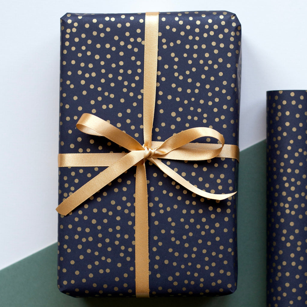 Navy blue gift box with gold polka dots and a gold ribbon on a green and white background