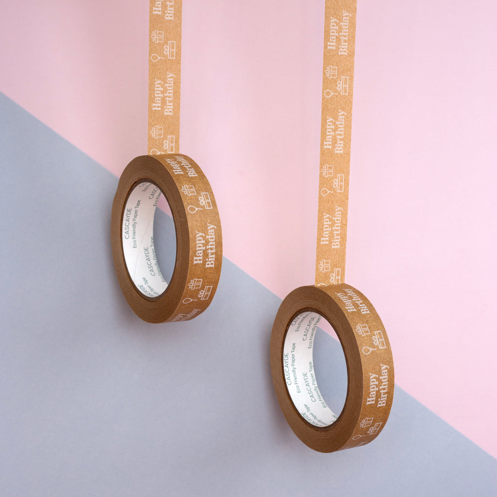 Two rolls of brown tape with 'Happy Birthday' text on a pink and gray background
