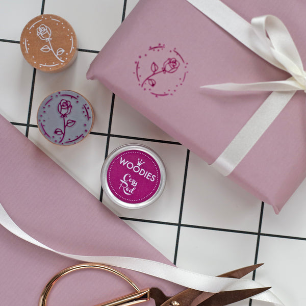 Pink wrapped gift with white ribbon, wooden and stamped wiith rose stamp and dark red ink on a checkered background.