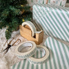 Decorative tape with tree pattern on a wooden dispenser and striped paper next to a Christmas tree.